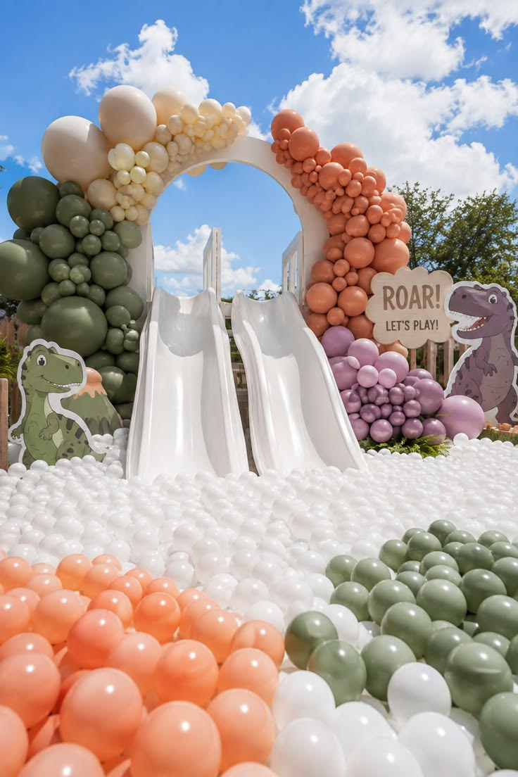 White ball pit and slide framed by green, peach and cream balloon arrangements