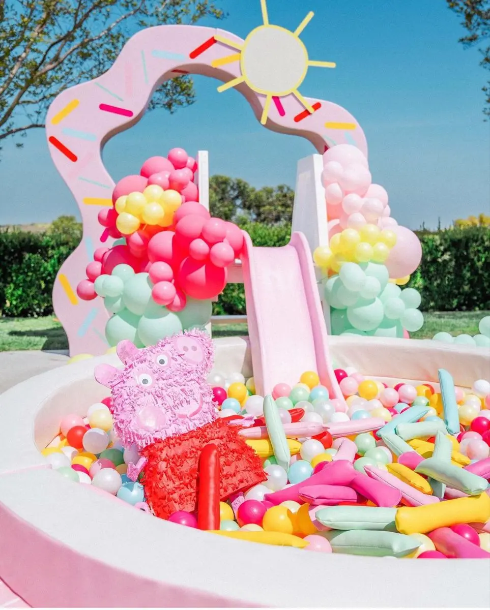 Pastel pink ball pit and slide beneath a rainbow balloon arch