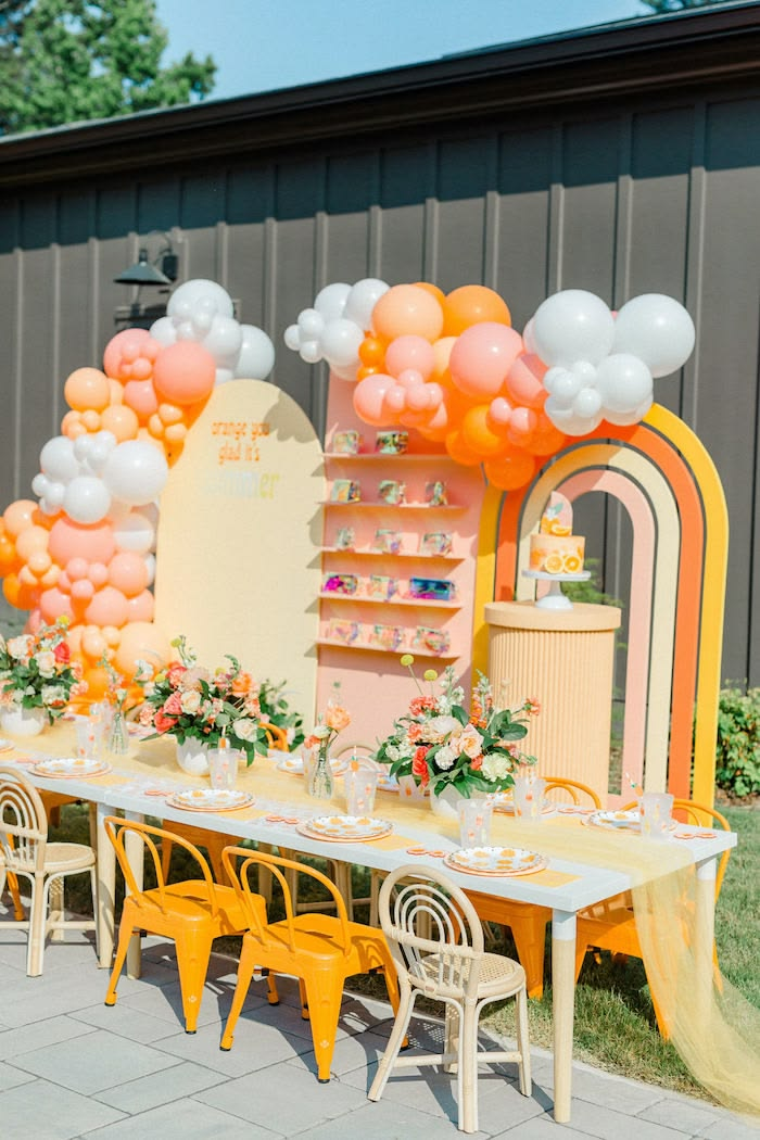 Orange and yellow kids' table with balloon garland, rainbow arch and flower centerpieces