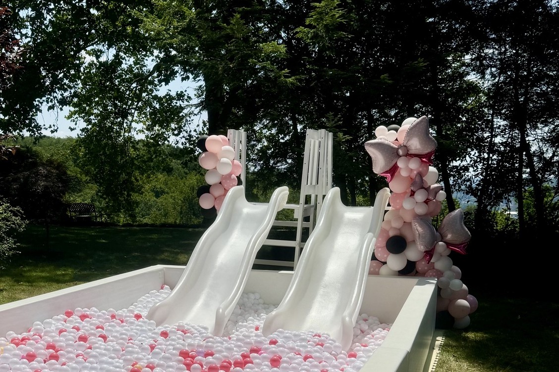 Pale pink, black and rose-gold balloon columns framing two white slides above a ball pit