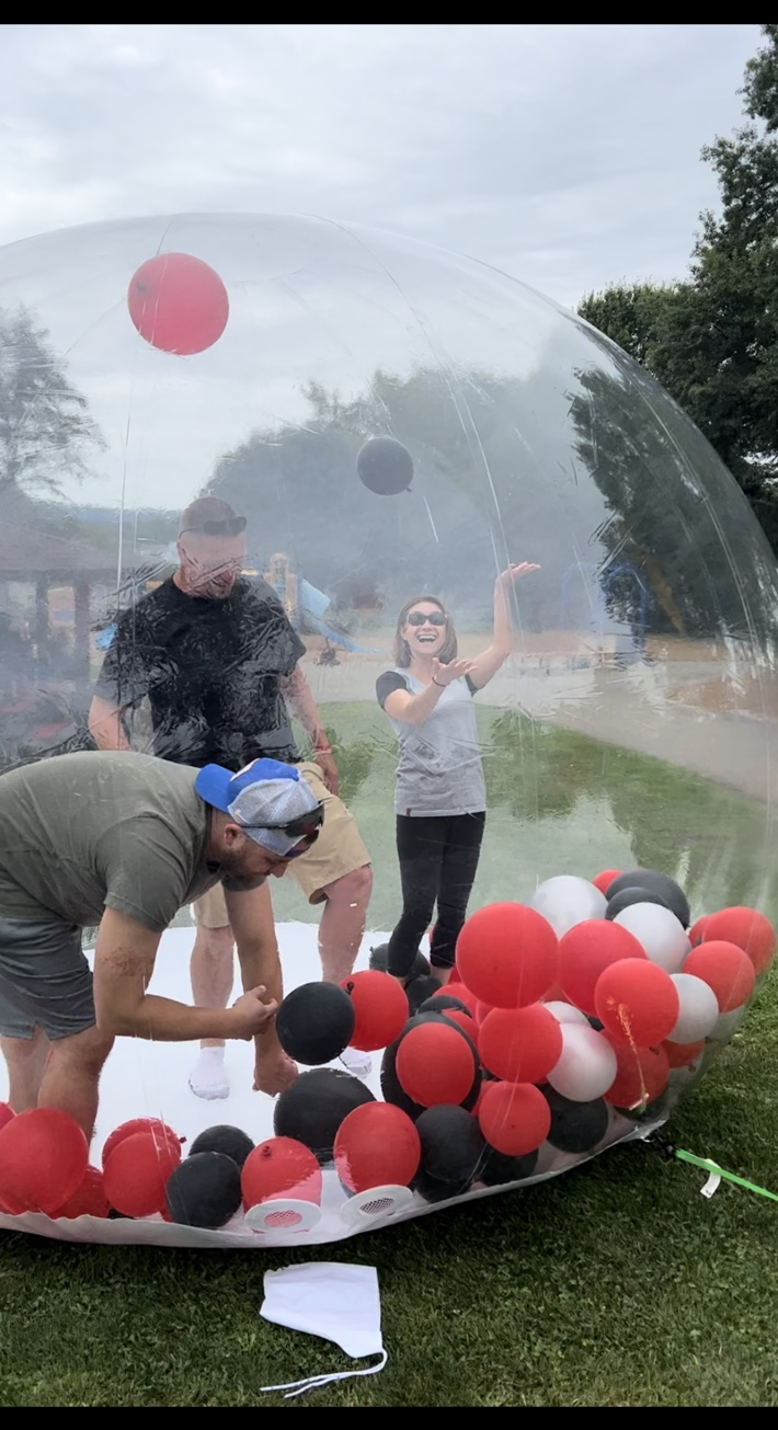 Guests laughing inside a large clear inflatable balloon dome filled with red, black and white balloons